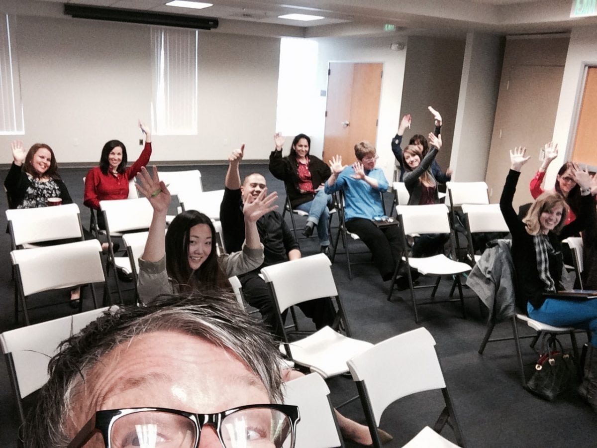 Tina Taking A Selfie Picture With Students Raising Their Hands In The Background Inside A Classroom Discussing Instagram For Businesses
