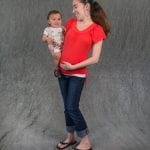 an image of a woman in a red shirt holding her small child and touching her pregnant belly