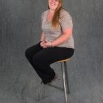 an image of a woman in a gray shirt sitting on a stool and smiling