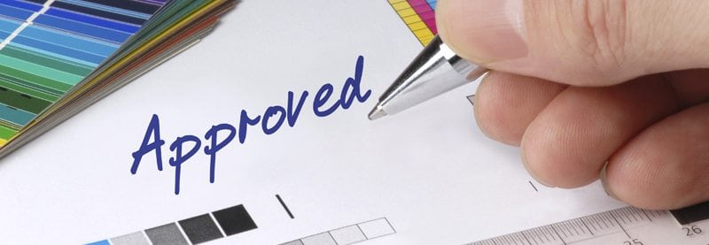 a close up image of a hand holding a pen writing the word "Approved"