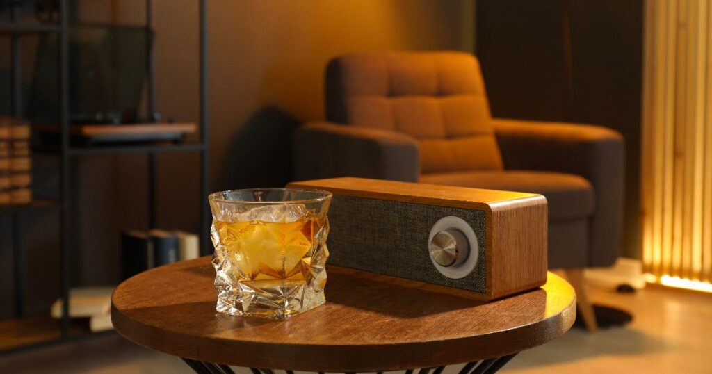 A cozy room with an arm chair and a small table with a wooden radio and whiskey resting on top.