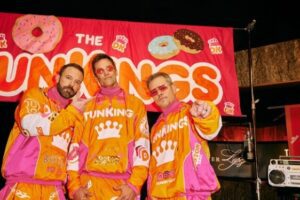 Three guys in yellow track suits in front of a Dunkin Donuts sign