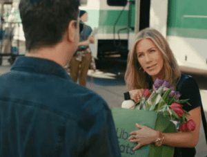 Jennifer Aniston talking to someone while holding a paper bag of groceries.