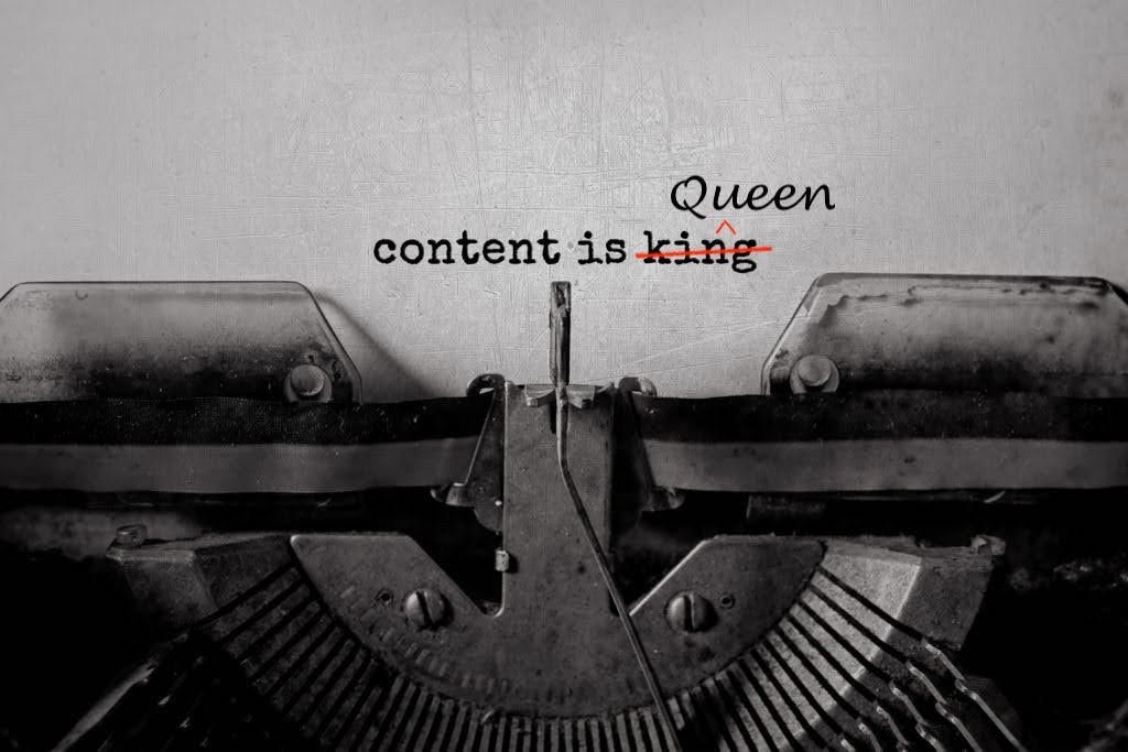 An image of a typewriter close up on the mechanical arms typing the words content is king with king crossed and queen written above in a script font