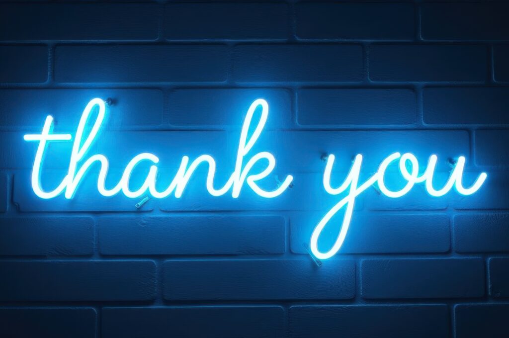 Bright neon sign saying thank you glowing against a dark brick background