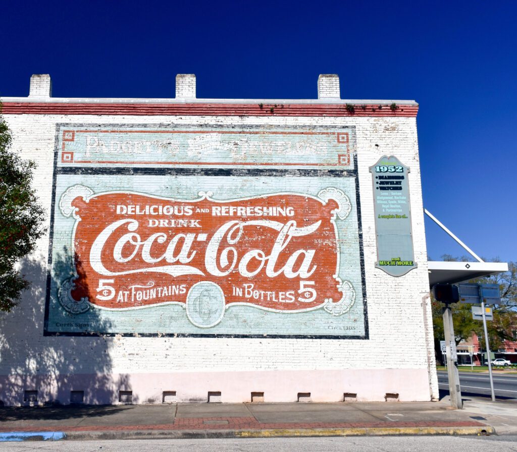 A painted sign on a wall outside of a building with the Coca-Cola logo