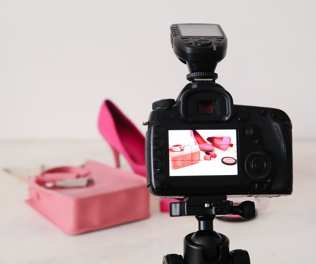 A photo of a DSLR camera on a tripod mount photographing pink shoes and a pink purse on a white seamless backdrop